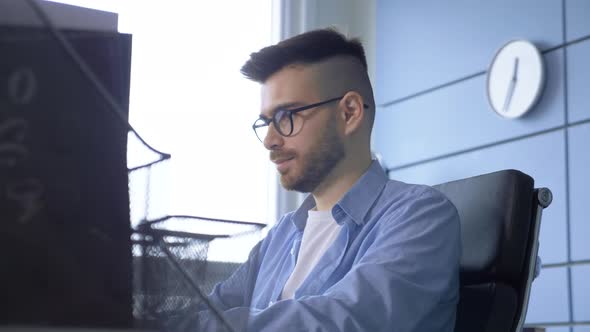 young businessman works at laptop sitting at the table in home office alt