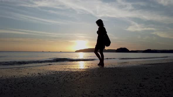 Woman on a sandy beach in the evening in Thailand cleaning her shoes in the ocean alt