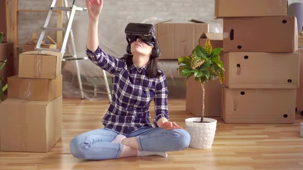 Portrait of a Young Woman in Virtual Reality Glasses Sitting on the Floor Next To the Boxes alt
