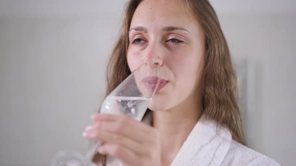 Closeup of Happy Smiling Young Woman with Bridal Bouquet Drinking Champagne Standing in Bathroom alt