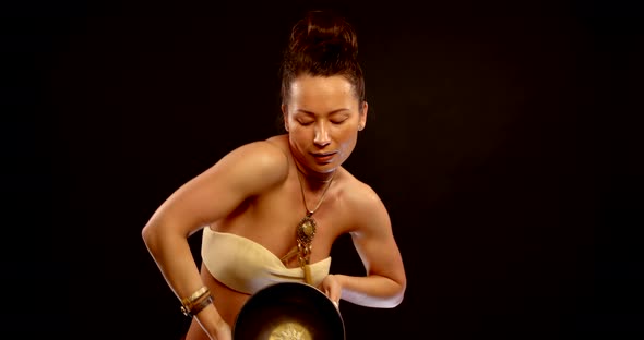 Pretty Woman Is Dancing with Bronze Traditional Tibetan Bowl in Black Background alt