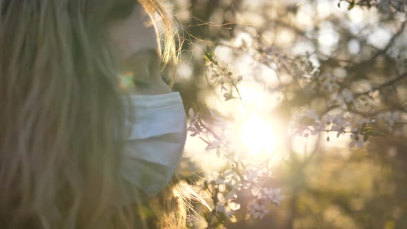 Girl in a Medical Mask Sniffs a Flowering Tree at Sunset Close-up alt