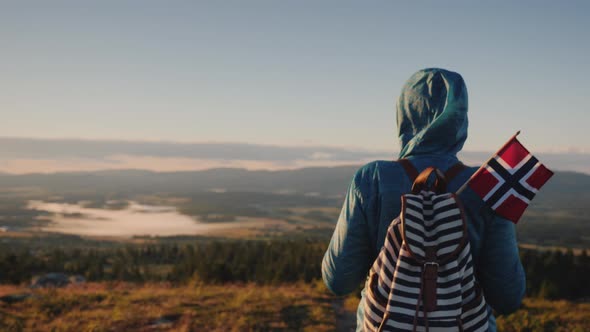 A Woman with a Backpack and a Norwegian Flag Is Walking Along the Picturesque Mountain Trail alt