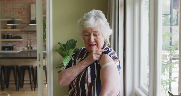 Happy caucasian senior woman showing plaster on arm after covid vaccination alt