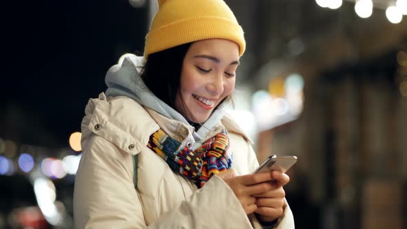 Woman standing at the night street, holding mobile phone.