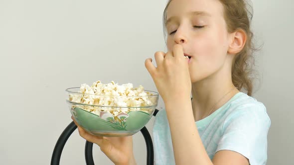 Portrait of a Funny and Excited Schoolgirl Girl on a White Background Smiling and Eating Popcorn alt