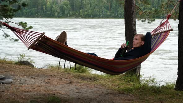 Man Drinking Beer While Resting in a Hammock alt