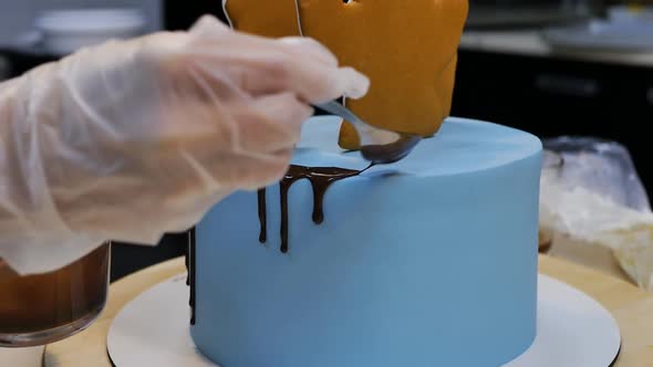 Pastry Chef's Hands Pour Chocolate From a Spoon on a Blue Cake Making Streaks