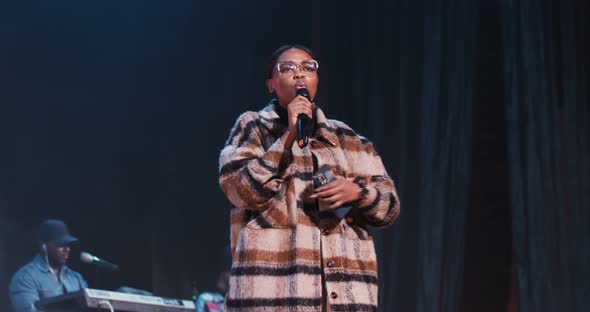 AfricanAmerican Woman Sings Into a Microphone As She Walks Around the Stage alt