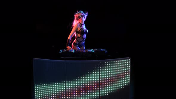 DJ Blonde Woman in Neon Light Behind the Decks alt
