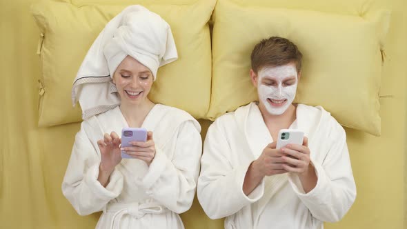 Attractive Lady and Guy Lie on Bed Together Using Smartphones