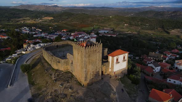 A drone captures a flock of birds flying past the Belmonte Castle tower as the sunsets. alt