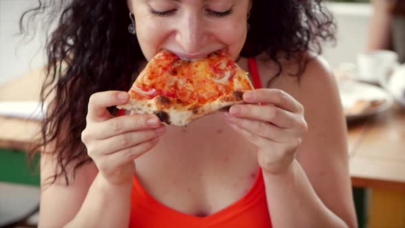 Young Cute Italian-looking Woman in a Red Dress Eagerly Eating and Enjoying Italian Pizza While in a alt