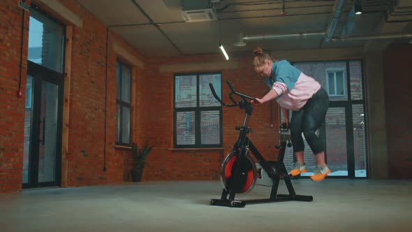 Athletic Woman Ride on Spin Stationary Bike Training Routine in Haze Gym Weight Loss Indoors alt