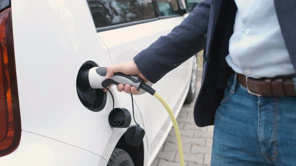 Man Coming to the Electric Car and Plugging in a Charging Cable alt