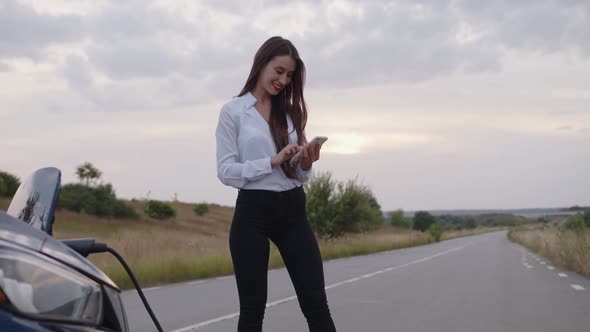 Woman Stands on the Road and Looks in Her White Phone alt