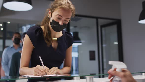 Caucasian woman in face mask has hands disinfected by male colleague at office reception desk alt