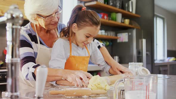 Grandmother and little girl in apron flattening dough with rolling pin  alt