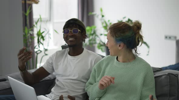 Happy Biracial Couple Sitting on Sofa with Laptop and Cellphone Congratulating Each Other alt