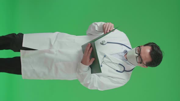 Asian Doctor With Stethoscope Wearing Mask, Reading Document While Walking On Green Screen alt