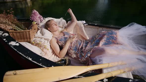 Woman daydreaming on sunny day laying down in a traditional rowboat, static shot alt