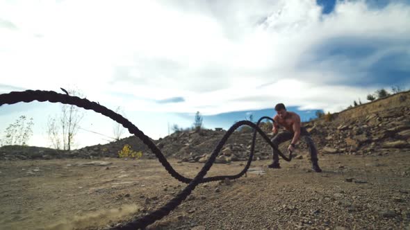 Sportsman exercising with battle ropes outdoors. Strong athlete doing double and alternating wave ex alt