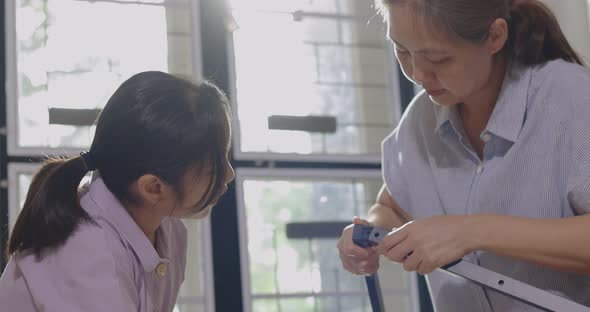 Asian Woman And Daughter Move To New Home Assembling Furniture Together, Daughter Helps Mother. alt