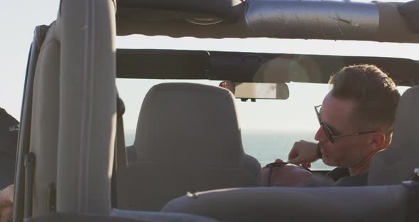 Happy caucasian gay male couple in car relaxing with feet out of window on sunny day at the beach alt