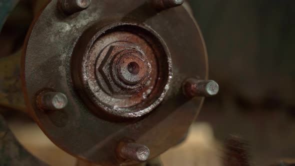 An Auto Mechanic Cleans a Spacer on a Car Hub From Rust with a Metal Brush with a Drill Before alt