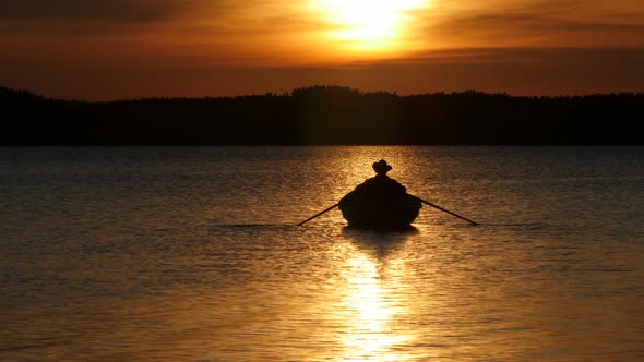 Golden Sunset Over Lake and Silhouette of Fisherman Rowing on Boat