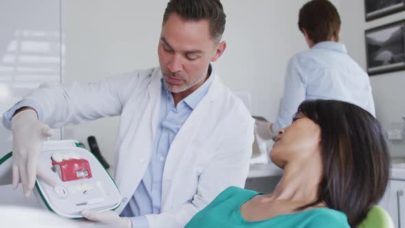 Caucasian male dentist with dental nurse examining teeth of female patient at modern dental clinic alt
