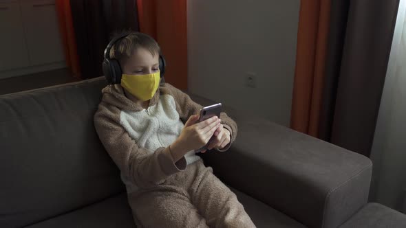 The Guy in the Protective Mask Sits on the Couch Listening To Music in Headphones. Quarantine 2020