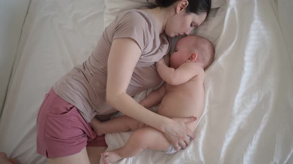 Young Mother Lying with Newborn Cute Infant Naked Baby Boy on Bed Holding Him on Arms Hugging and