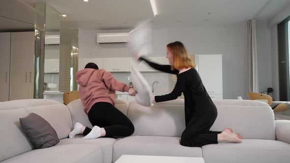 Two Young Girls Fight Pillows and Have Fun in the Living Room on the Couch