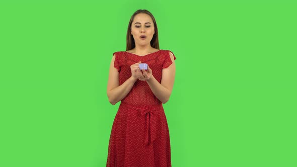 Tender Girl in Red Dress Is Opening a Small Box with a Surprise and Is Very Rejoicing, Saying Yes alt