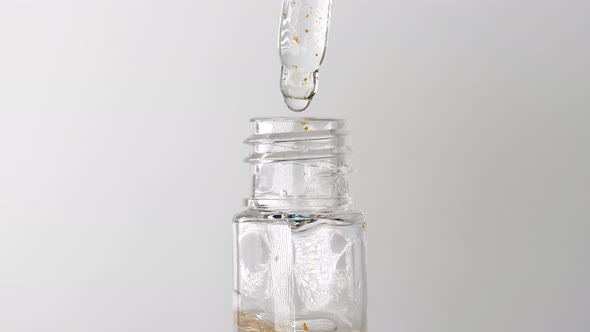 Serum with Gold Drops Falling From the Cosmetic Pipette on White Background alt