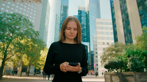 Lady Uses Smartphone App Walking in Paris Downtown with Skyscrapers Outside