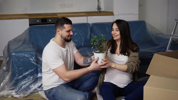 Smiling Couple Sitting on the Floor in the Living Room Unpacking Plant From the Box alt