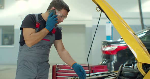 Mechanic Talking on a Mobile Phone with the Car Owner While Repairing a Car in a Garage