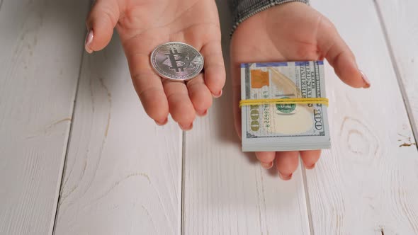 Closeup of a Bitcoin and a Stack of Hundred Dollar Bills in the Hands of a Woman alt