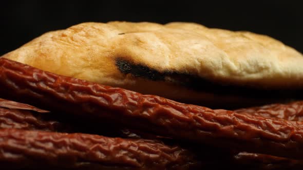 Delicious Mediterranean flatbread with traditional smoked sausage rotates against a black background