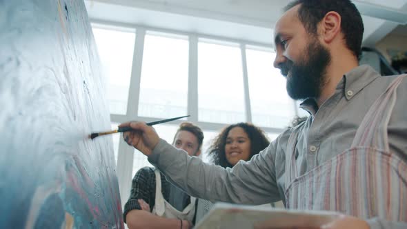 Skilled Adult Artist Painting Picture and Talking To Mixed Race Group of Students in Studio alt