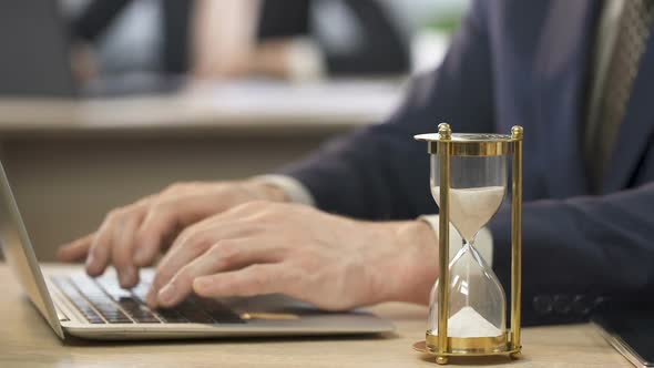 Man in Suit Working on Laptop at Office, Hourglass Standing on The Table, Time alt