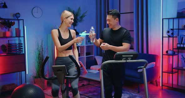 Woman and Asian Man which Drinking Water from Bottles During Evening Home workout alt