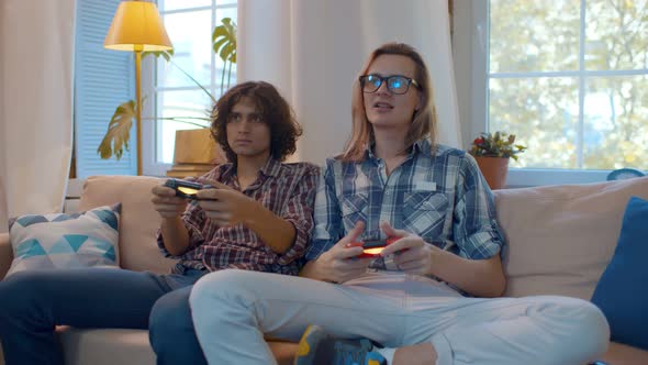 Young Cheerful Guys Playing on Console Sitting on Couch at Home alt