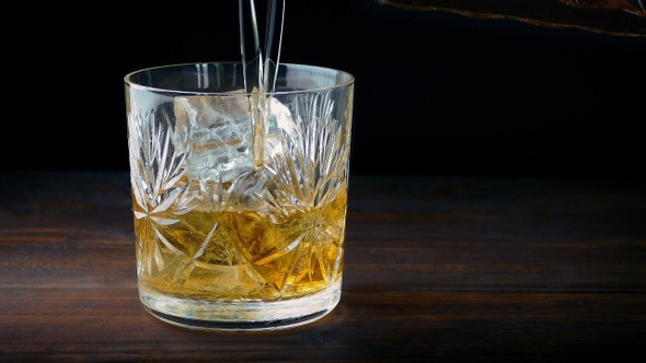 Whiskey Is Poured Over Ice Cubes In Glass alt