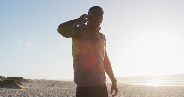 African american man checking smartwatch, exercising outdoors by seaside alt