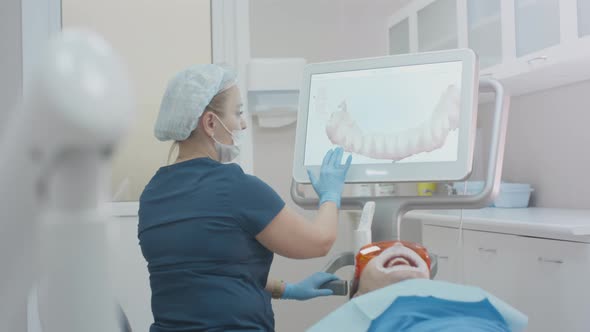 Girl Doctor Dentist Demonstrates a 3D Model of Teeth on a Touch Monitor alt