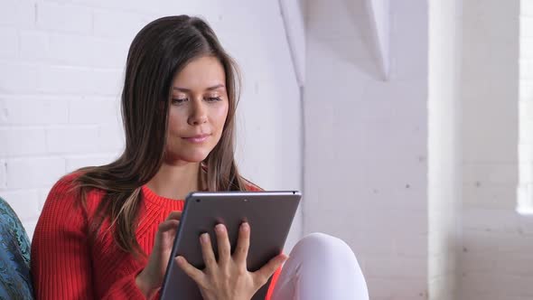 Attractive Young Female Sitting In Front Of A White Brick Wall While Playing On Her  Tablet 2