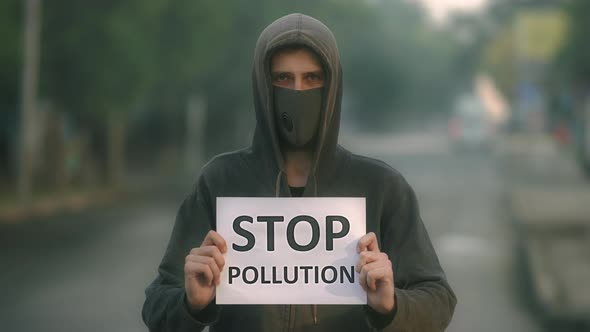 Man in Respiratory Mask Look at Camera Backdrop Road with Banner Stop Pollution alt